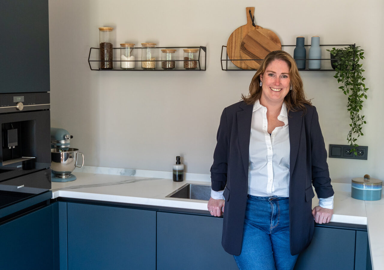 Foto van Daniëlle Cortjens in een moderne keuken met donkerblauwe fronten en een wit marmer werkblad.